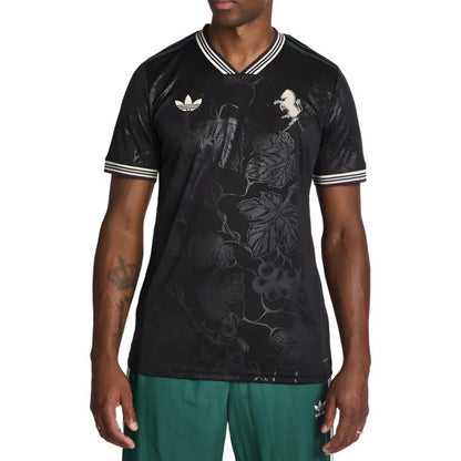 A man wearing a black short-sleeve V-neck t-shirt with a subtle floral vine pattern, featuring white striped trim on the collar and cuffs, and a white trefoil logo on the chest.