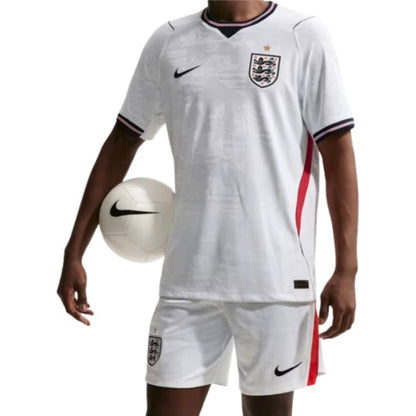 A soccer player wearing a white England national team jersey and matching shorts, holding a white soccer ball against a plain white background.