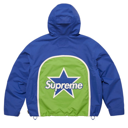 A blue hooded jacket shown from the back, featuring a large green panel with a white border and a central star containing the Supreme logo.